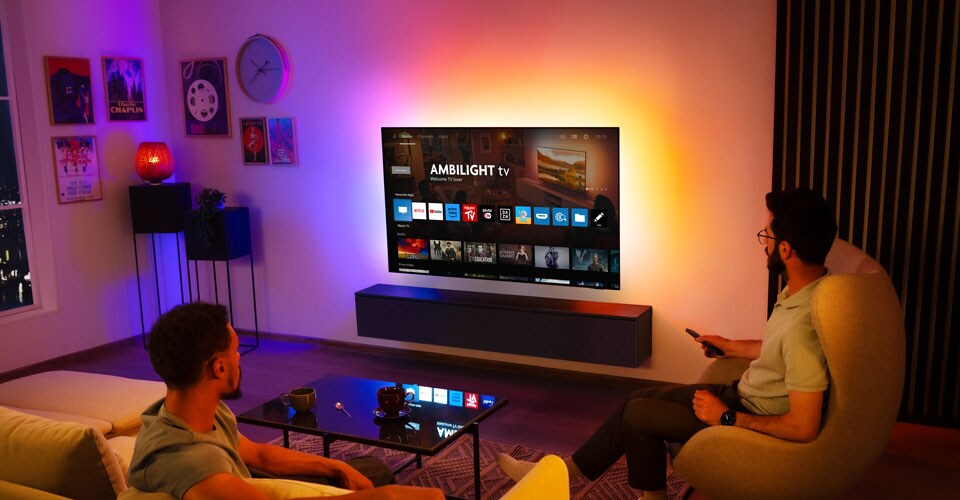 Dois homens assistem a uma TV Ambilight montada na parede em uma sala de estar